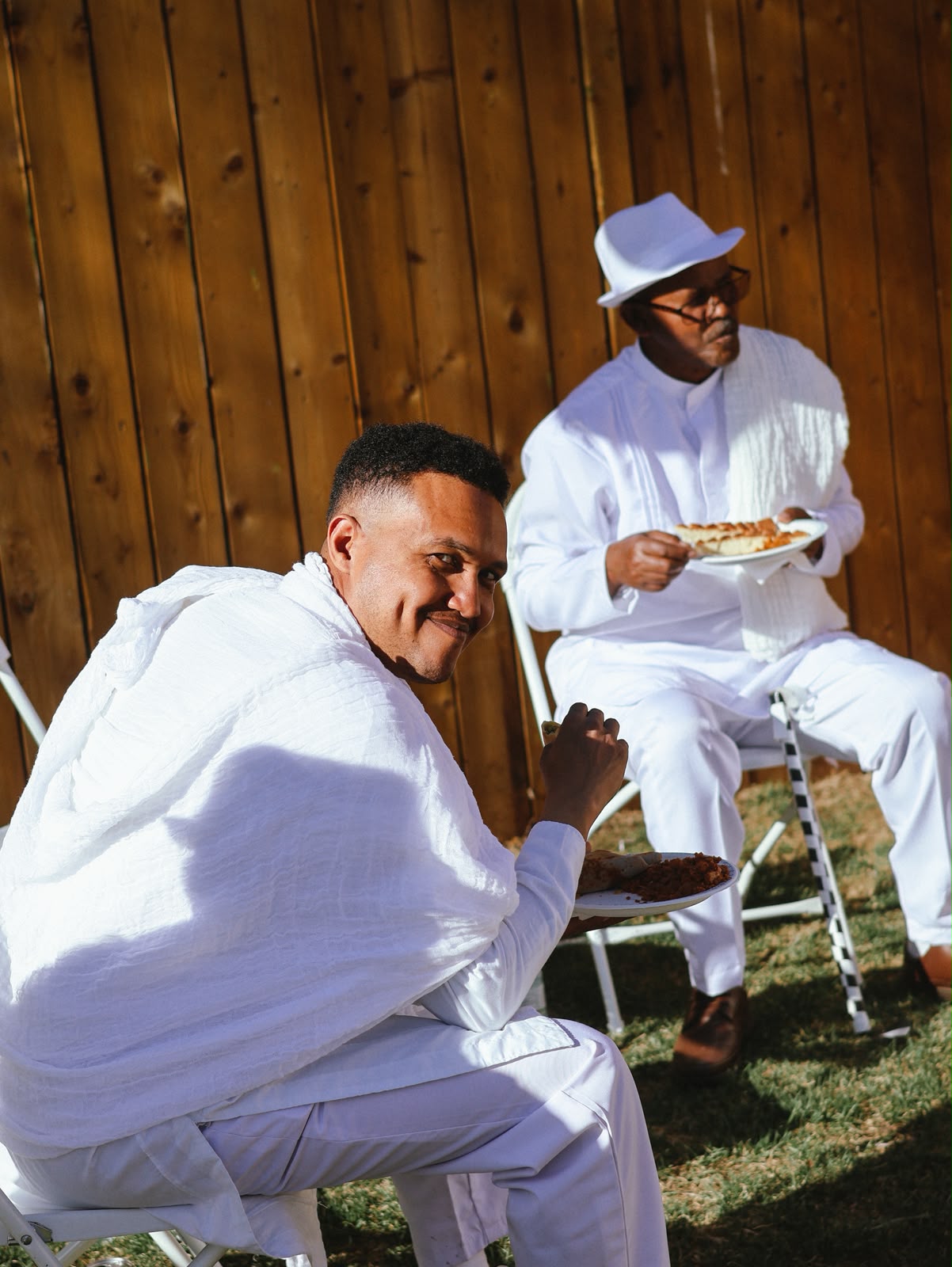 Two men in white clothing seated, sharing a meal
