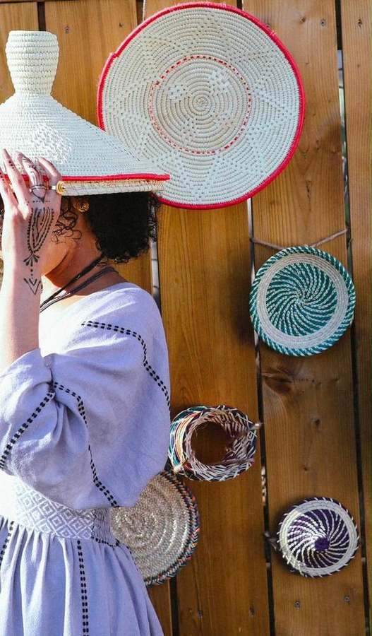 Woman holding a woven straw hat overhead beside hanging baskets