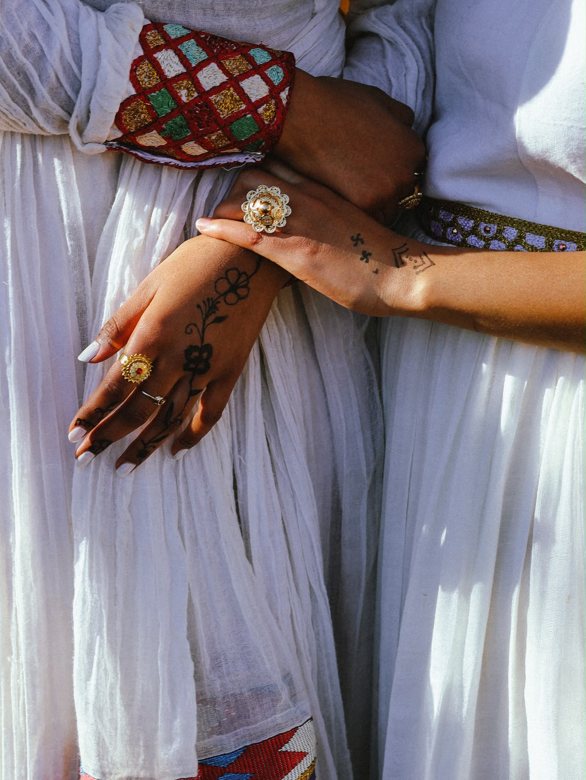 Detail of two hennaed hands crossed together, with rings and embroidered cuffs