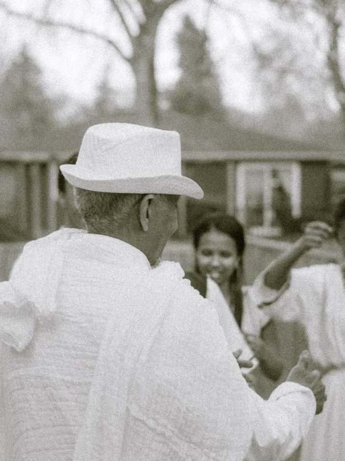 An elder in a white hat greeting others