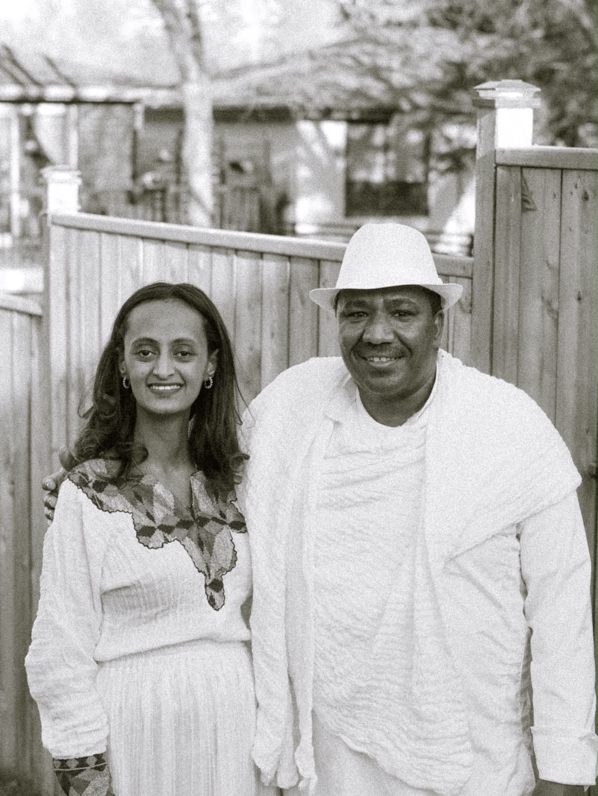 A young woman and a man in a white hat and shawl smiling together