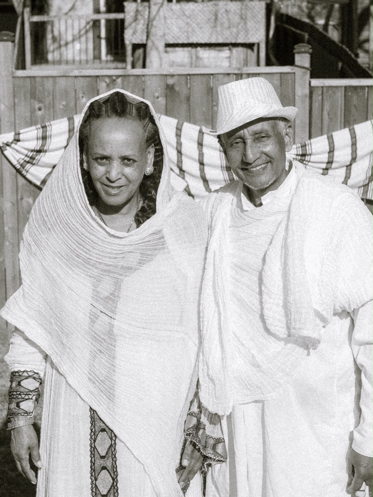 An elder woman in a headscarf and a man in a white hat smiling together