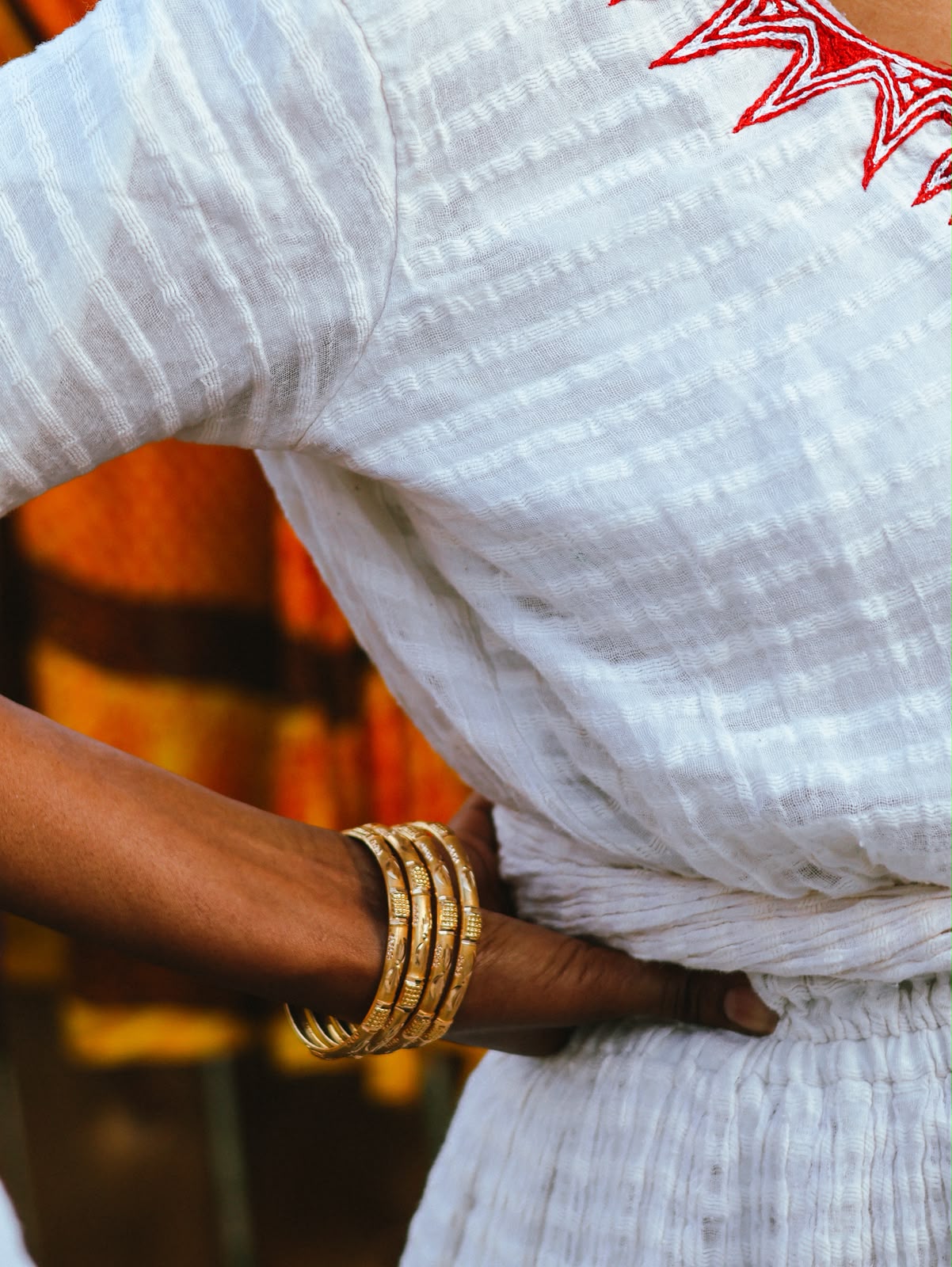 Detail of a gold bangle bracelet at the waist of an embroidered white dress