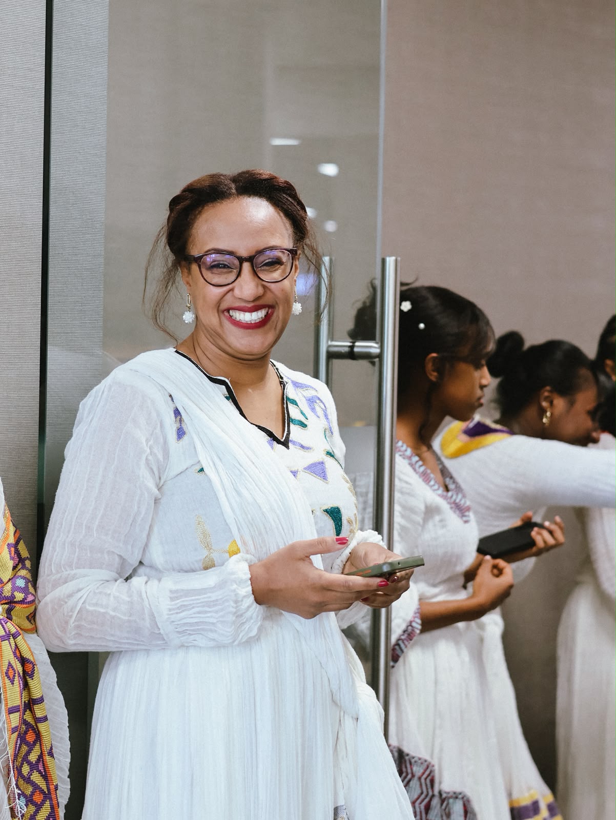 Woman in glasses smiling warmly in an embroidered white dress